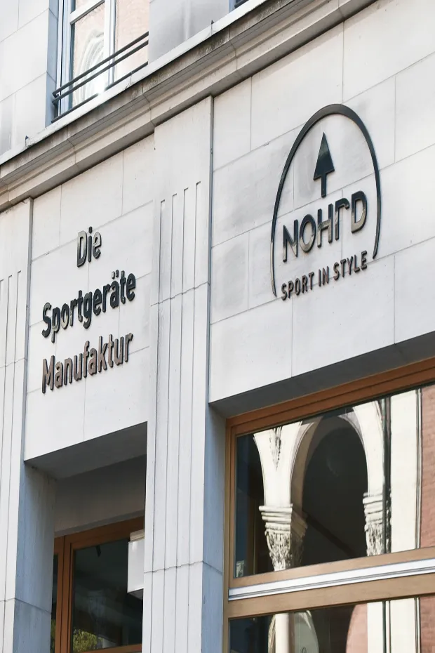 Schild mit der Aufschrift "Die Sportgeräte Manufaktur" und "NOHRD - Sport in Style" an einer Gebäudefassade.