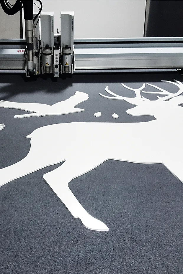Eine Schneidemaschine schneidet eine weiße Silhouette eines Rehs auf einem dunklen Untergrund.